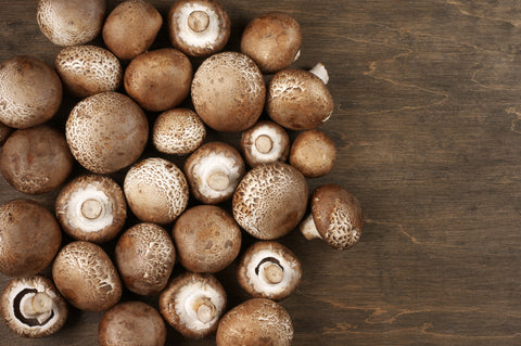 A bird's eye view of crimini mushrooms sprawled on a wooden table