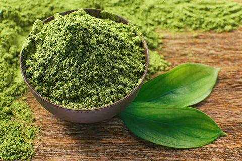 A bowl of powdered matcha on a wooden table, with two tea leaves